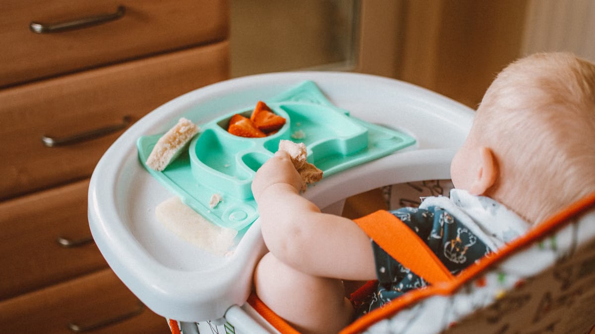 A cute baby enjoying snack time in a high chair with colorful food tray indoors.